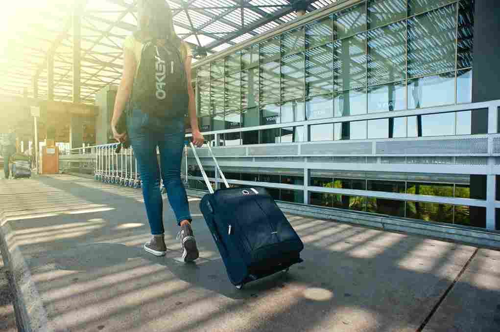 Mulher andando em um aeroporto com uma Mochila de Viagem nas costas e puxando uma mala de rodinhas.
